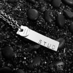 black rocks in the background with a silver chain necklace with a silver bar that reads STUD and a circle with an = sign on it