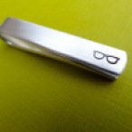 a silver tie bar with black etched glasses at the far right end sits on a bright green backdrop