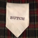 a white folded hankie is sitting on a plaid background with the word BUTCH embroidered in the center