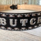 Black belt with silver stitching and accents reading BUTCH sits on a wooden surface